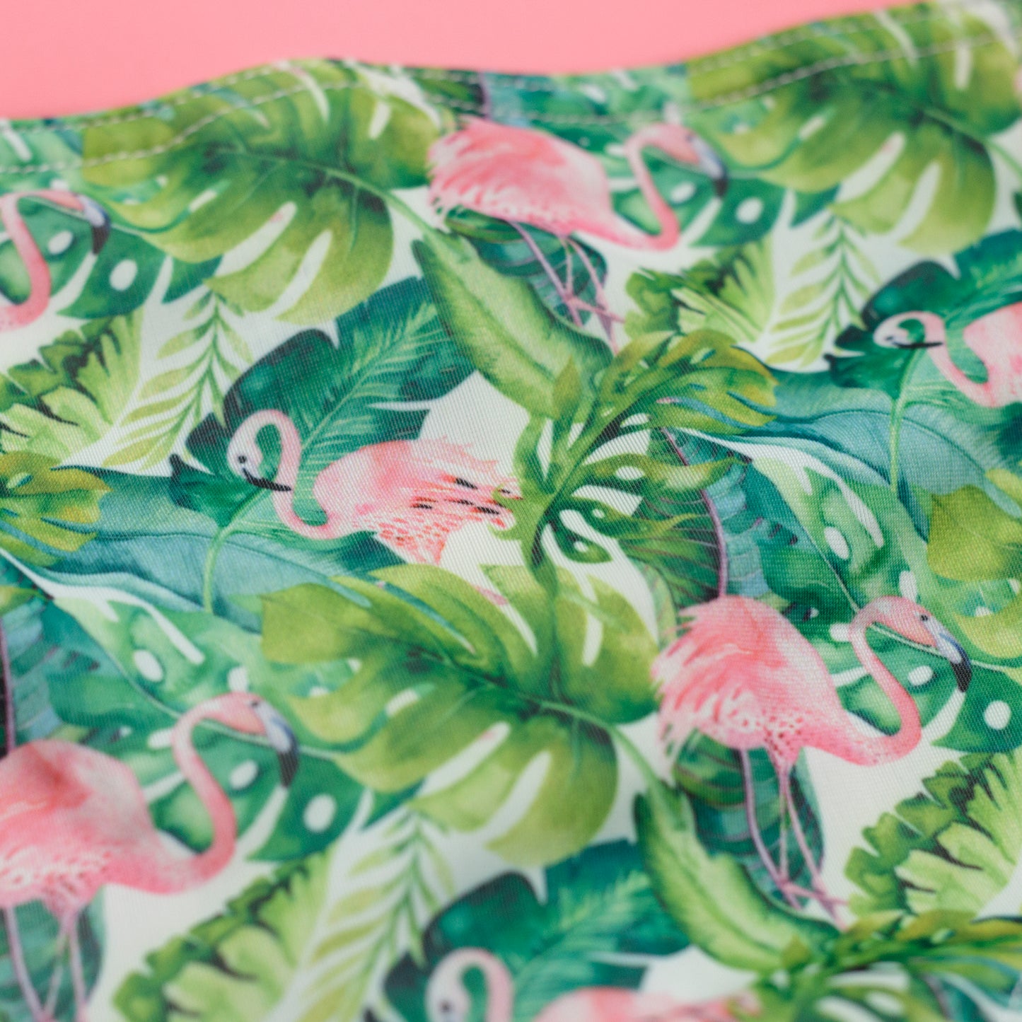 Zöld trópusi levelek és rózsaszín flamingó mintájú textil közelről fotózva, a kétrészes kislány bikini részlete
