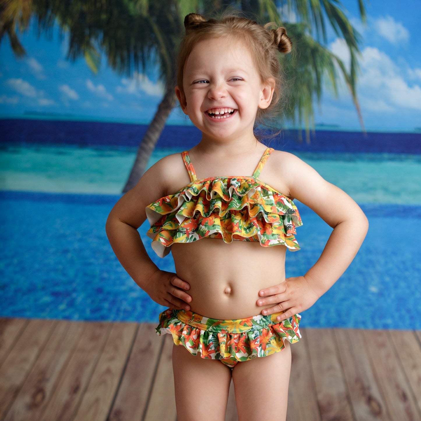 Hawaii virágos fodros kislány bikini szett, tengerpart mintájú háttér előtt fotózva modellen.