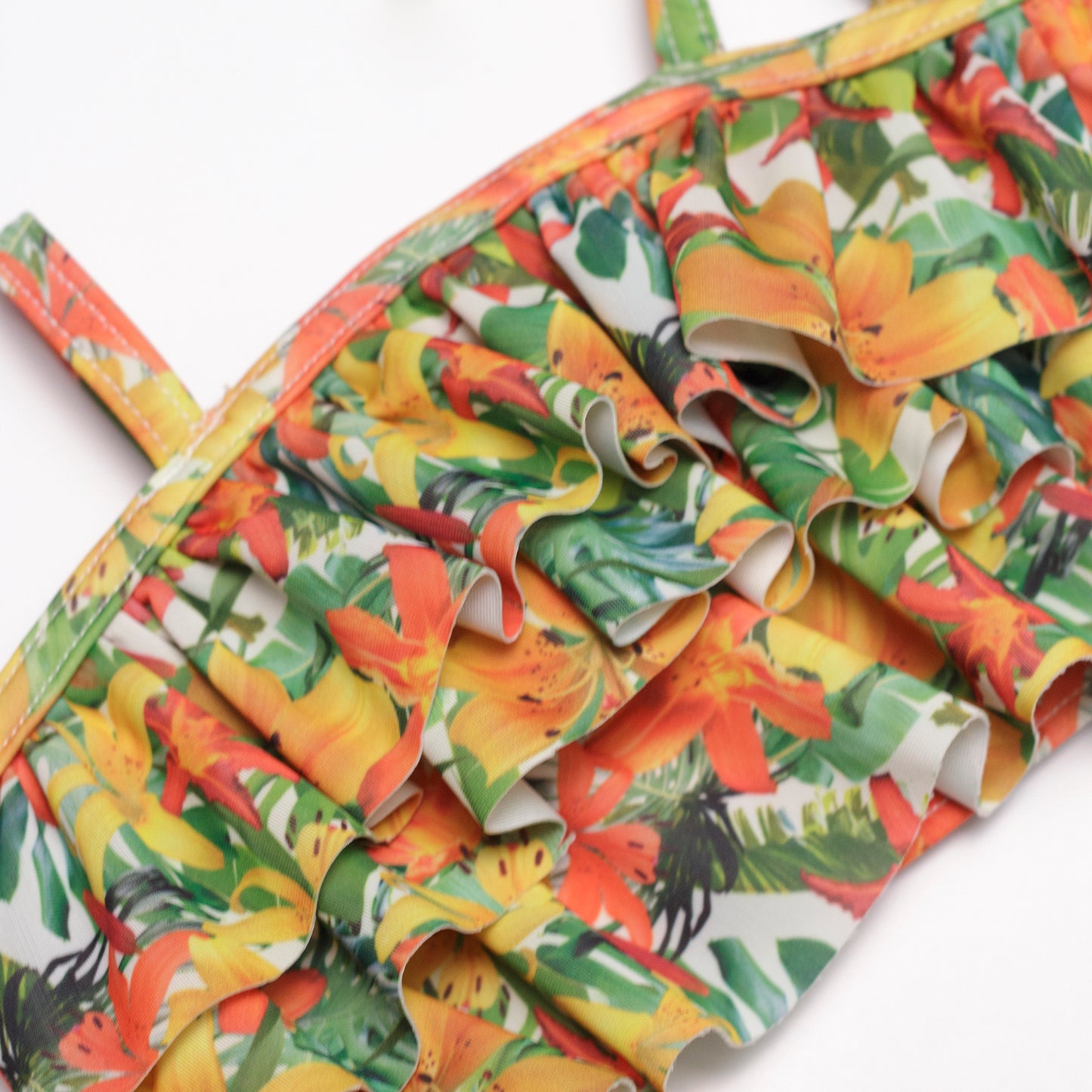 Hawaii virágmintás kislány bikini felső textil mintája és varrása közelről, jól láthatóan a fodrokkal, fehér alapon fotózva.