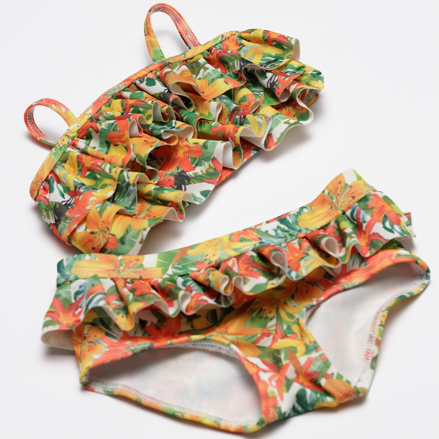 Fodros hawaii virág mintájú kislány kétrészes bikini szett ferdén közelebbről fotózva, fehér háttéren.