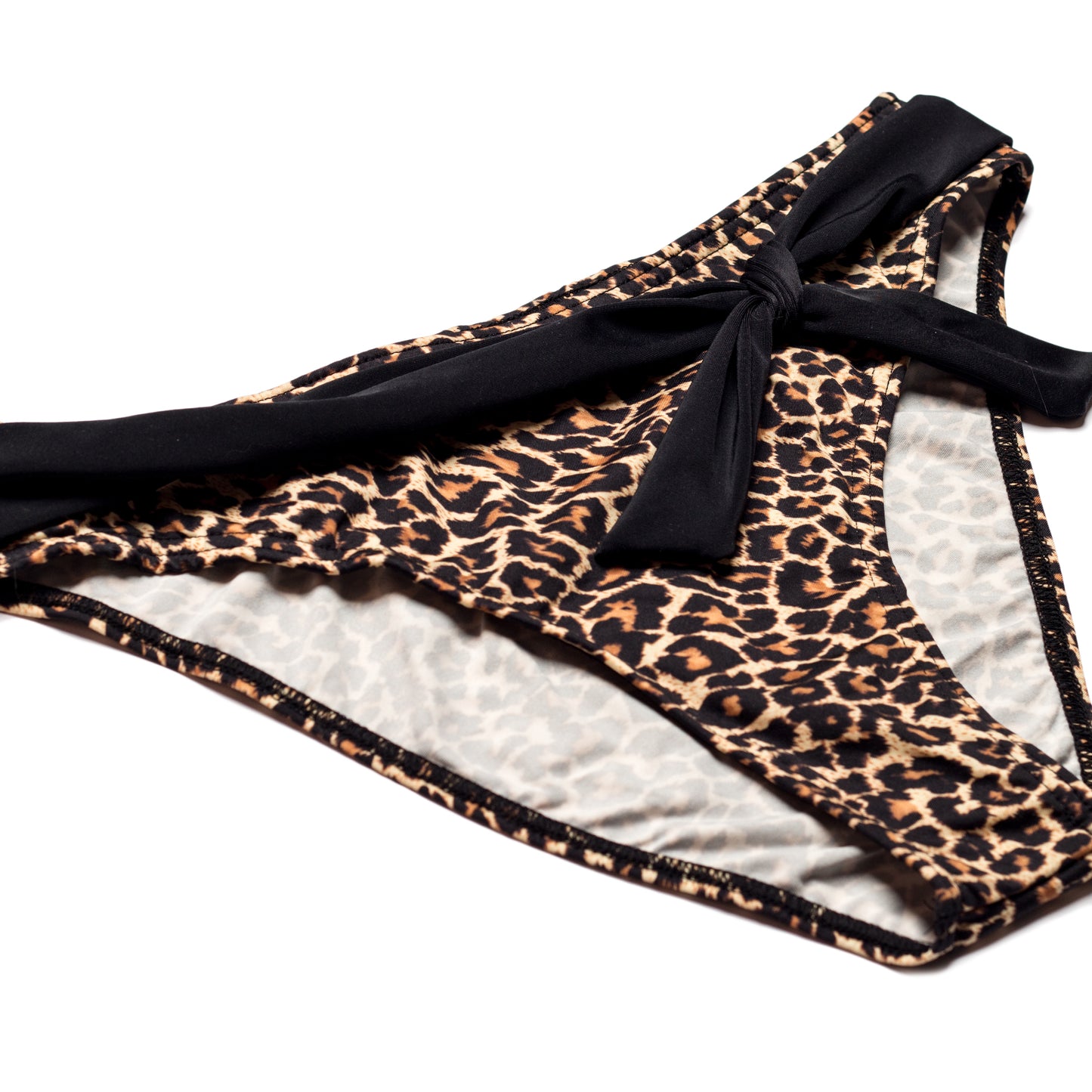 Leopárd mintás bikini alsó fekete megkötővel, oldalról és ferdén fotózva, fehér háttéren.