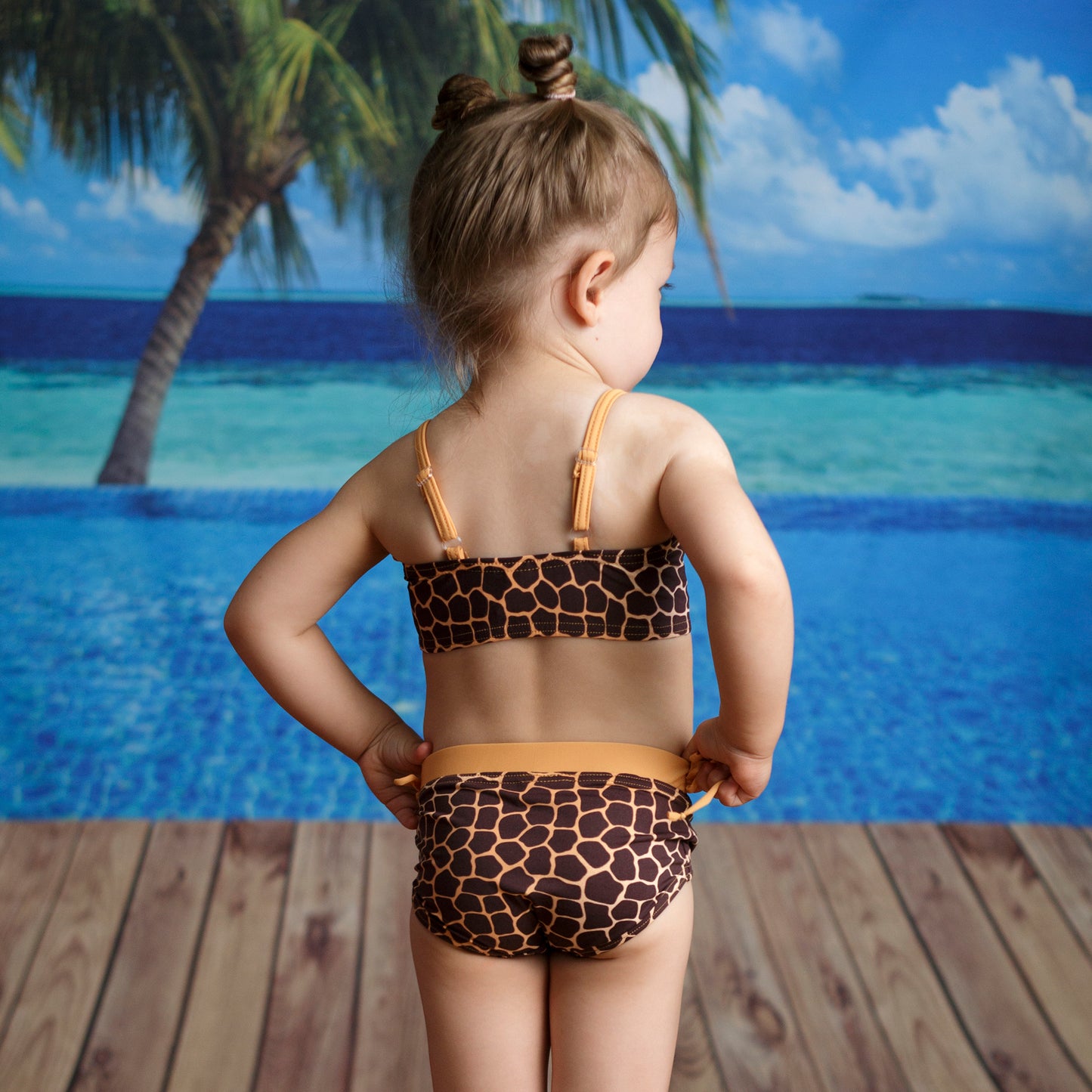 Zsiráf mintás kétrészes bikini szett modellen hátulról fotózva, tengerparti háttér előtt, állítható vállpántos felsővel és kontrasztos gumírozott derekú klasszikus alsóval.