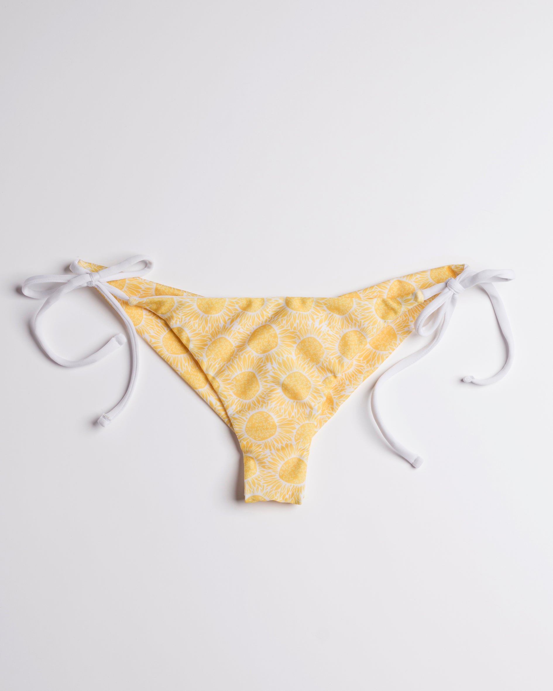 Napraforgó mintás brazil bikini alsó fehér megkötőkkel, leterítve, előről, fehér háttéren