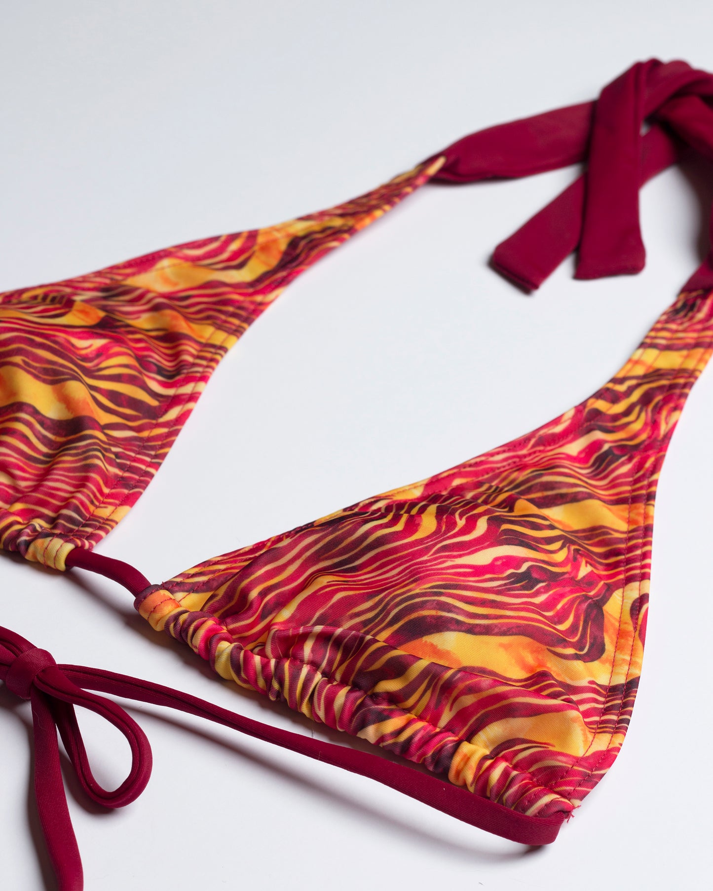 Részletfotó a Savanna bikini felső anyagáról és a bordó megkötőkről, fehér háttéren.